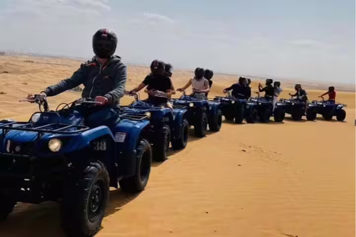 Group of adventurers riding quad bikes across stunning red desert dunes on an exhilarating safari tour experience.