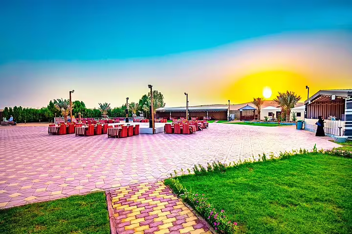 Vibrant desert safari camp at sunset with dining setup, lush greenery, and scenic views, ideal for a Red Dunes quad bike adventure.