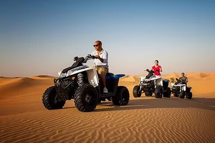Adventurers enjoying a thrilling quad bike ride across the scenic red dunes during a desert safari under clear blue skies.