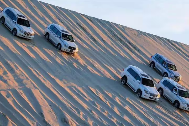 Convoy of SUVs descending vast desert dunes, showcasing exhilarating safari tour in the dunes.