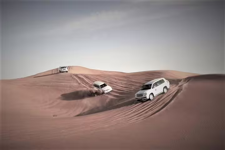 Three SUVs expertly maneuver over vast desert dunes, showcasing thrilling off-road adventure in a desert safari.