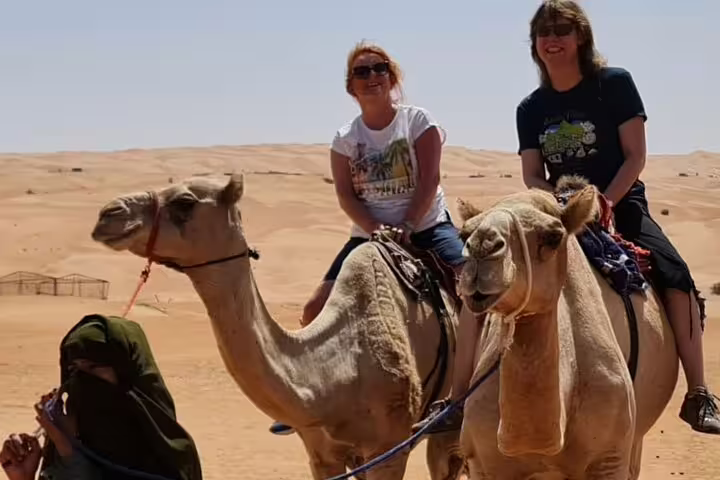Two travelers enjoying a camel ride across the picturesque desert landscape on a full day adventure tour.