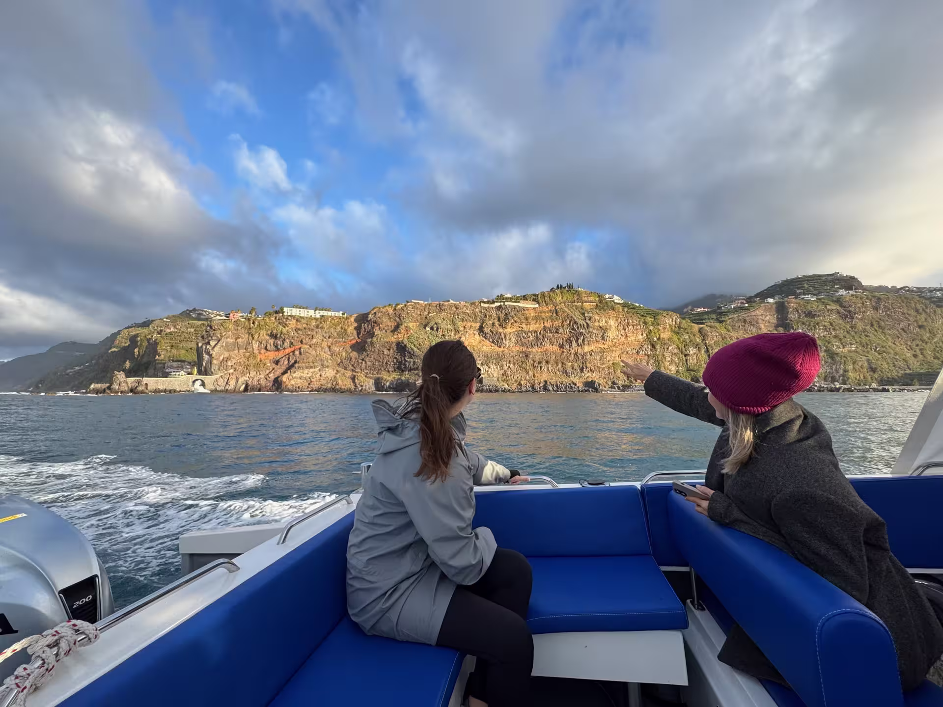 Two women on a boat admire the stunning coastal cliffs of Desertas Island, perfect for a scenic tour.