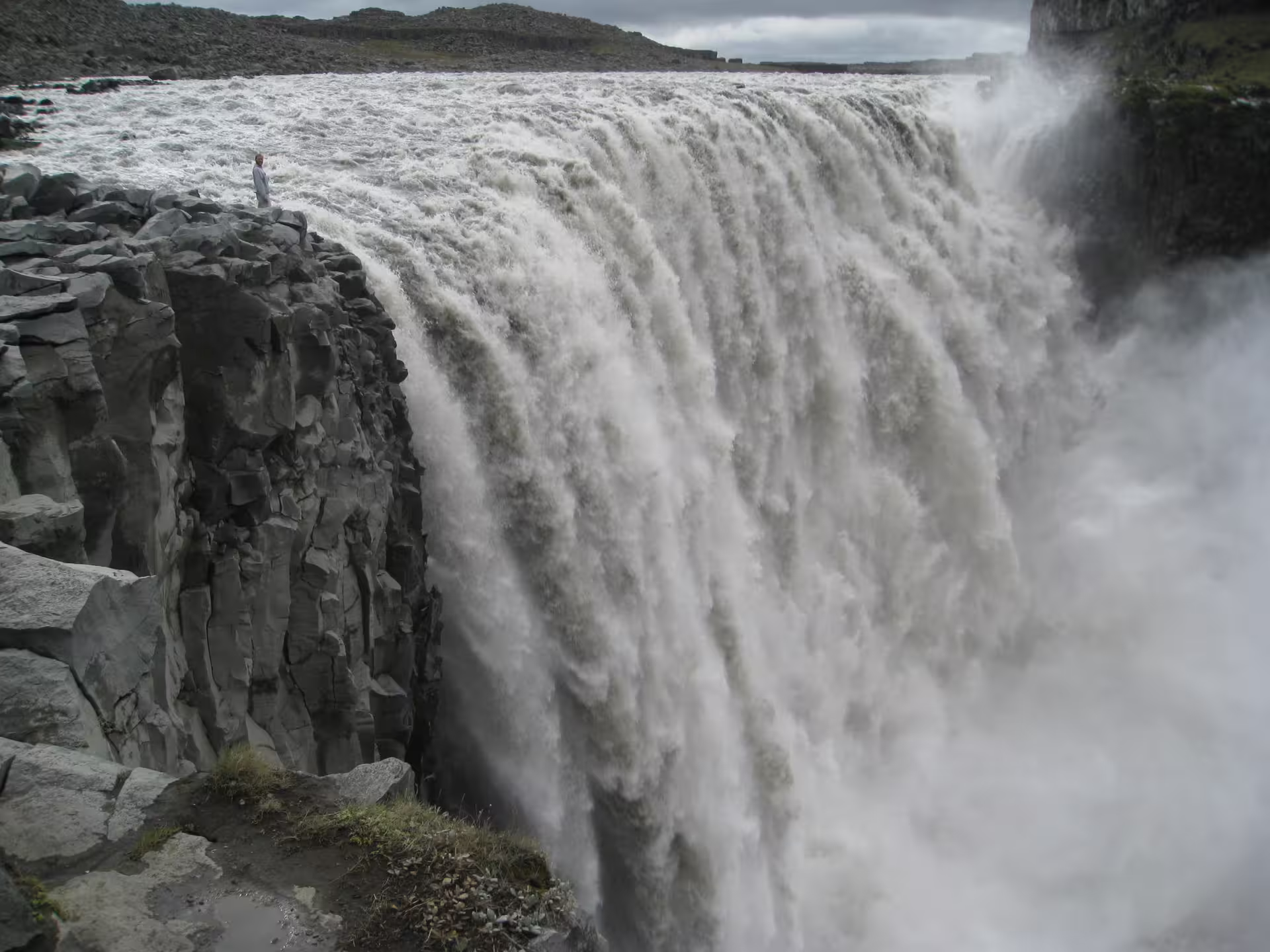 Person standing at edge of massive Dettifoss waterfall cliff in Iceland with powerful rushing water