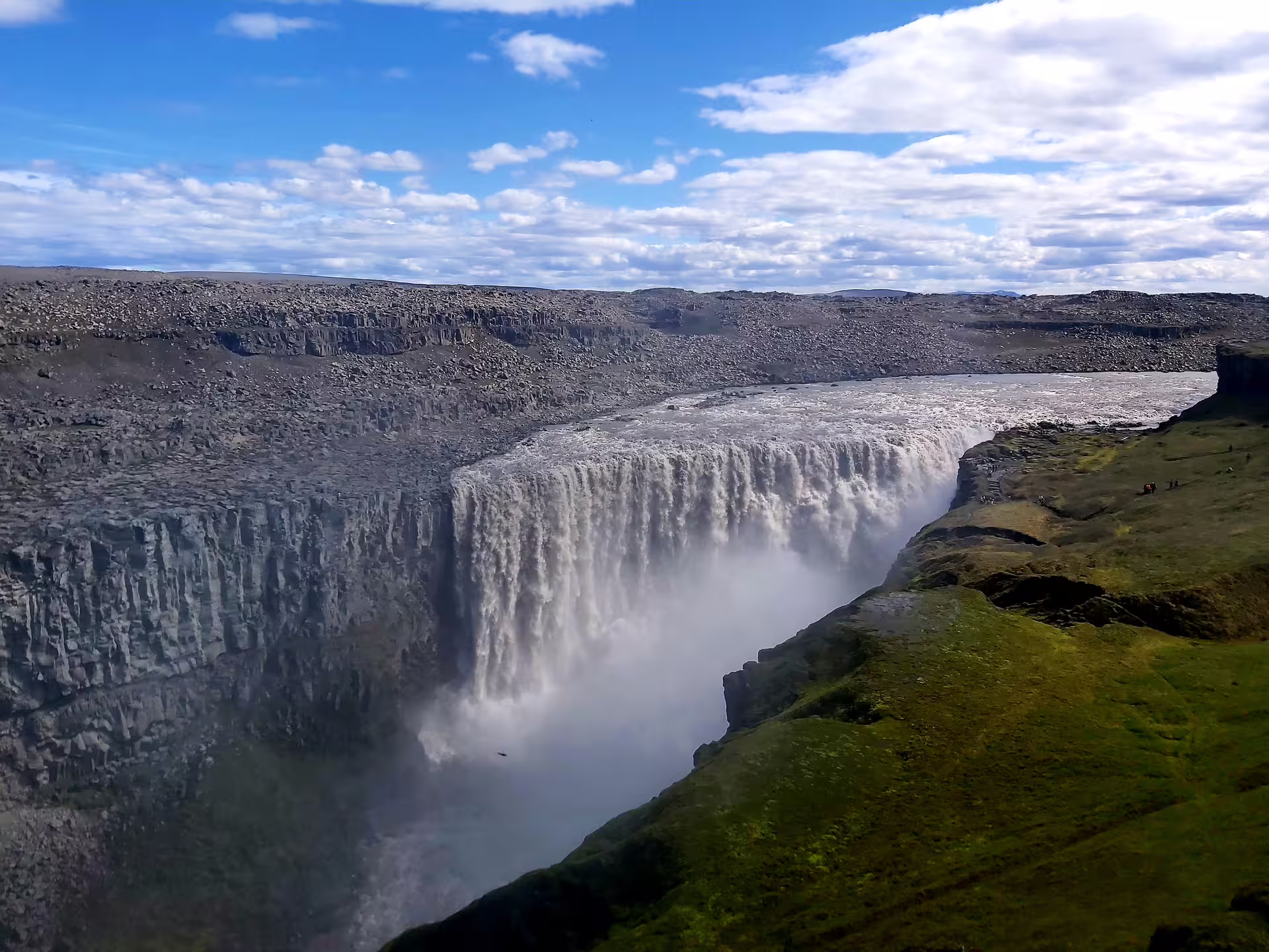 Dettifoss waterfall cascading into a misty canyon with green mossy cliffs and blue sky in Iceland