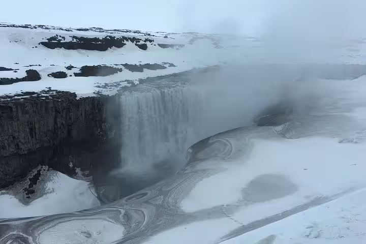 Snow-covered landscape with the powerful Dettifoss waterfall in Iceland, enveloped in mist and icy terrain.