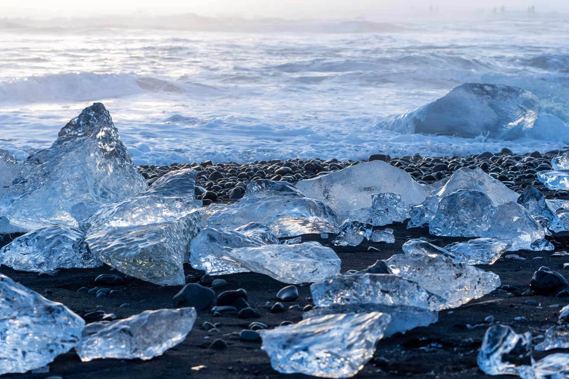 Crystal ice chunks scattered on black sand Diamond Beach with crashing Atlantic waves in Iceland