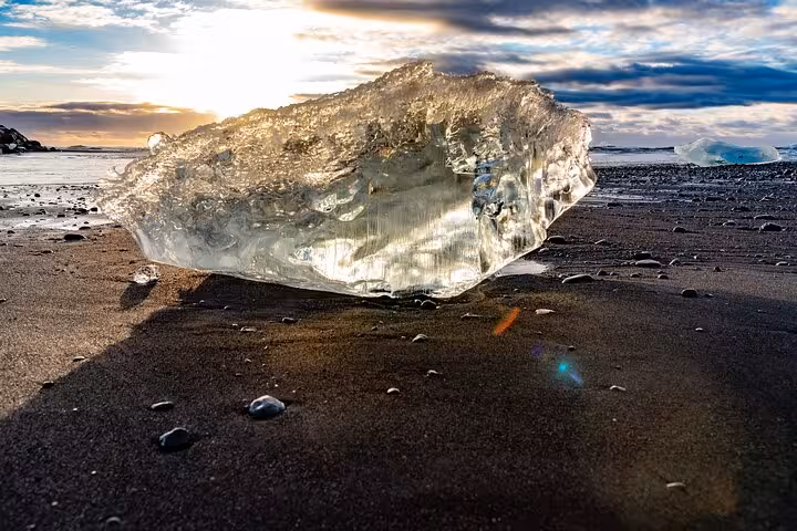 Large transparent ice chunk from Jokulsarlon glacier resting on Diamond Beach black sand at sunset