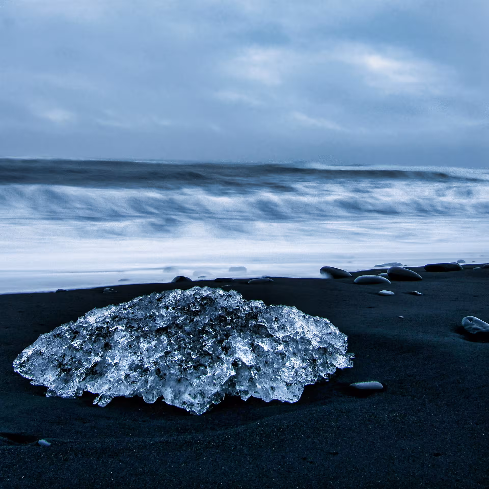 Large ice chunk washed ashore on black sand Diamond Beach with crashing waves and stormy sky