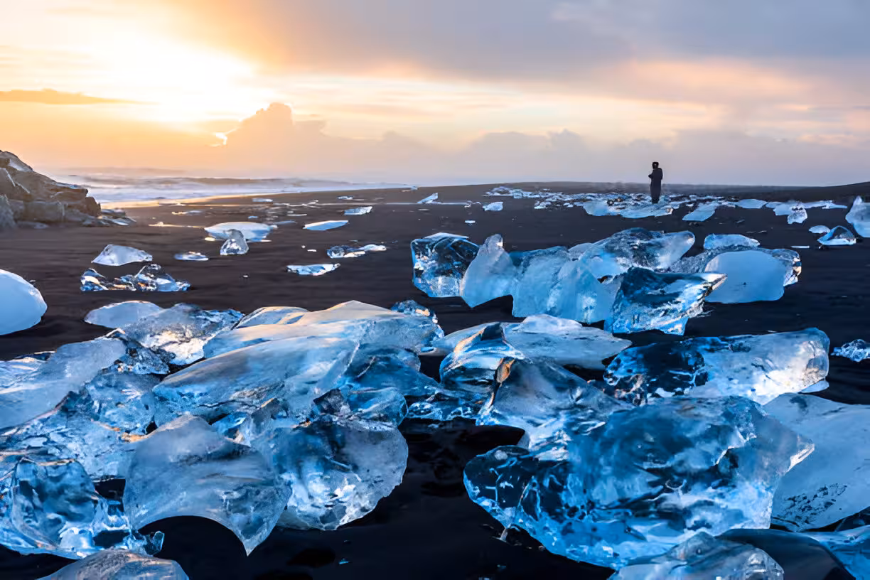 Ice chunks on Diamond Beach black sand with lone figure at sunset, South Coast Iceland