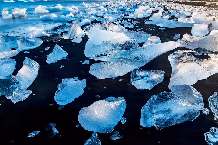 Translucent blue ice chunks scattered on black sand beach at Diamond Beach, Iceland
