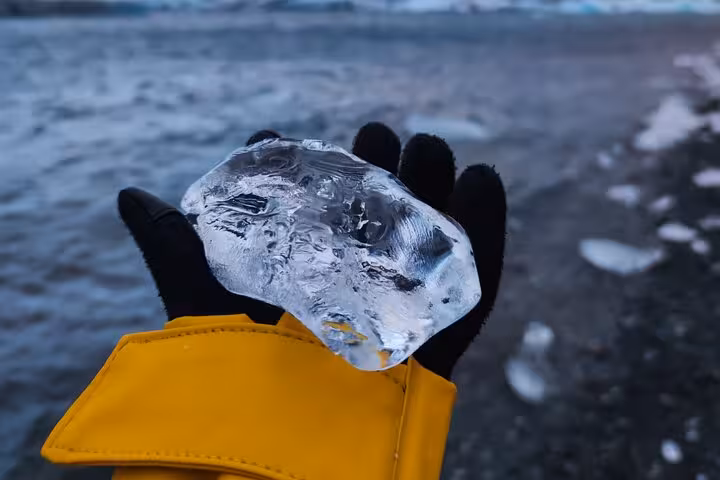 Hand holding a clear ice chunk at Diamond Beach, Iceland with glacier lagoon in background