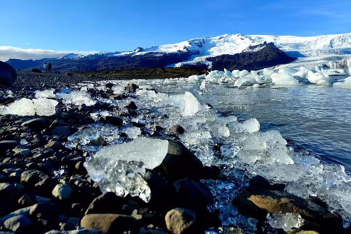 Ice chunks on black rocky shore of Diamond Beach with glacier lagoon and snow-capped mountains in Iceland