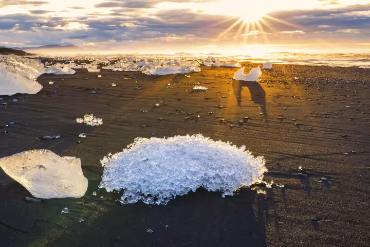 Ice chunks on black sand Diamond Beach Iceland at golden sunset with sunburst