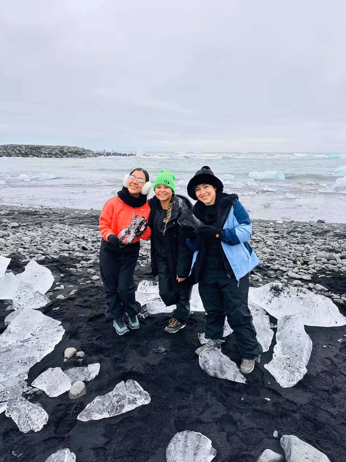 Three women posing on Iceland's Diamond Beach with ice chunks on black sand near the ocean