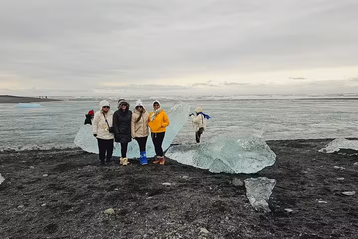 Group of tourists posing beside large ice chunks on Diamond Beach near Jokulsarlon Glacier, Iceland