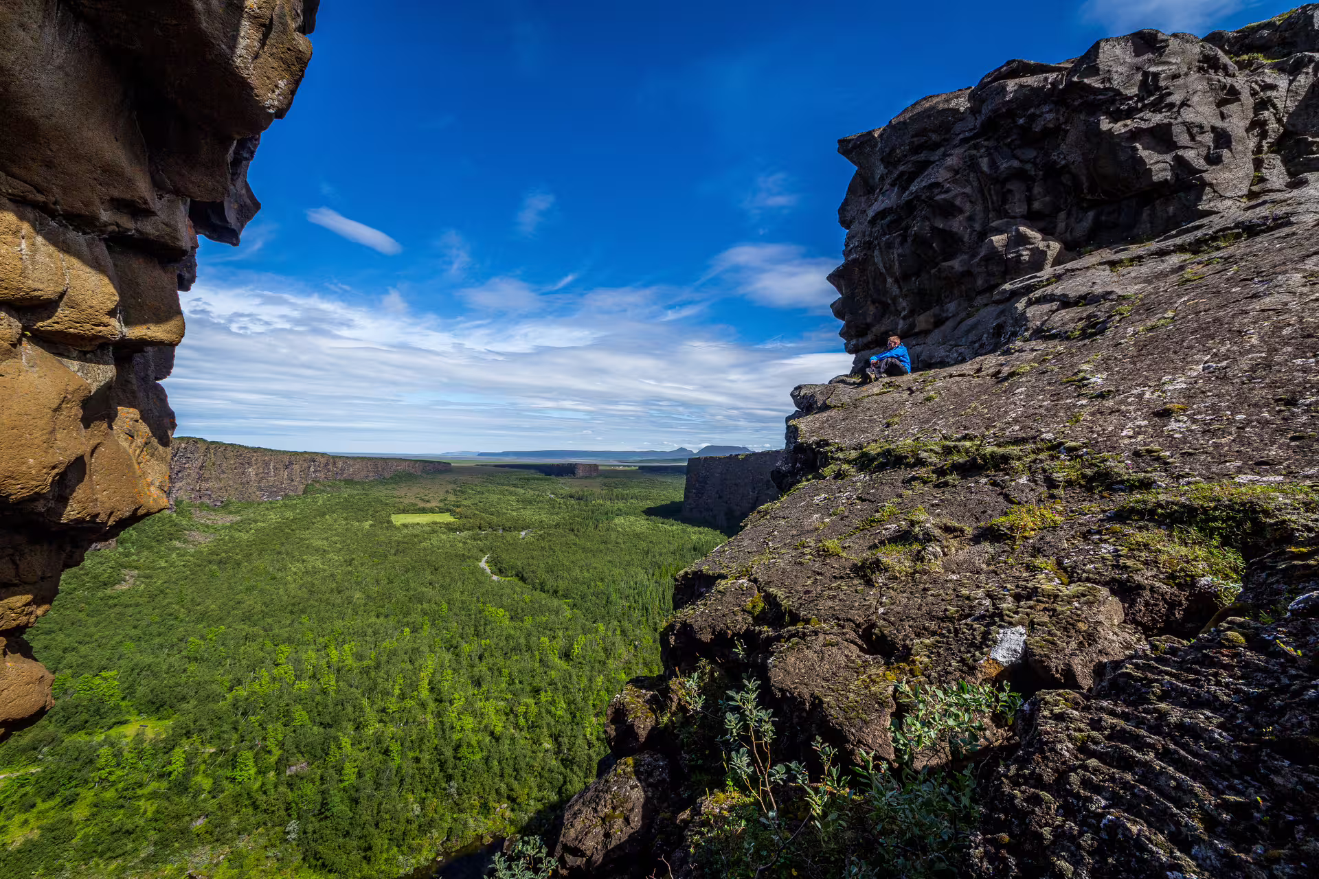 Hiker sitting on volcanic canyon rim overlooking lush green valley on Diamond Circle tour from Akureyri