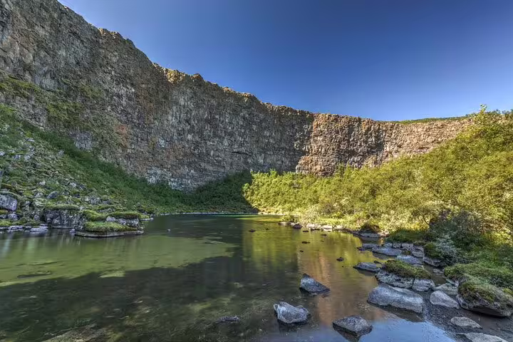 Calm green river pool surrounded by towering basalt cliffs and lush vegetation in North Iceland