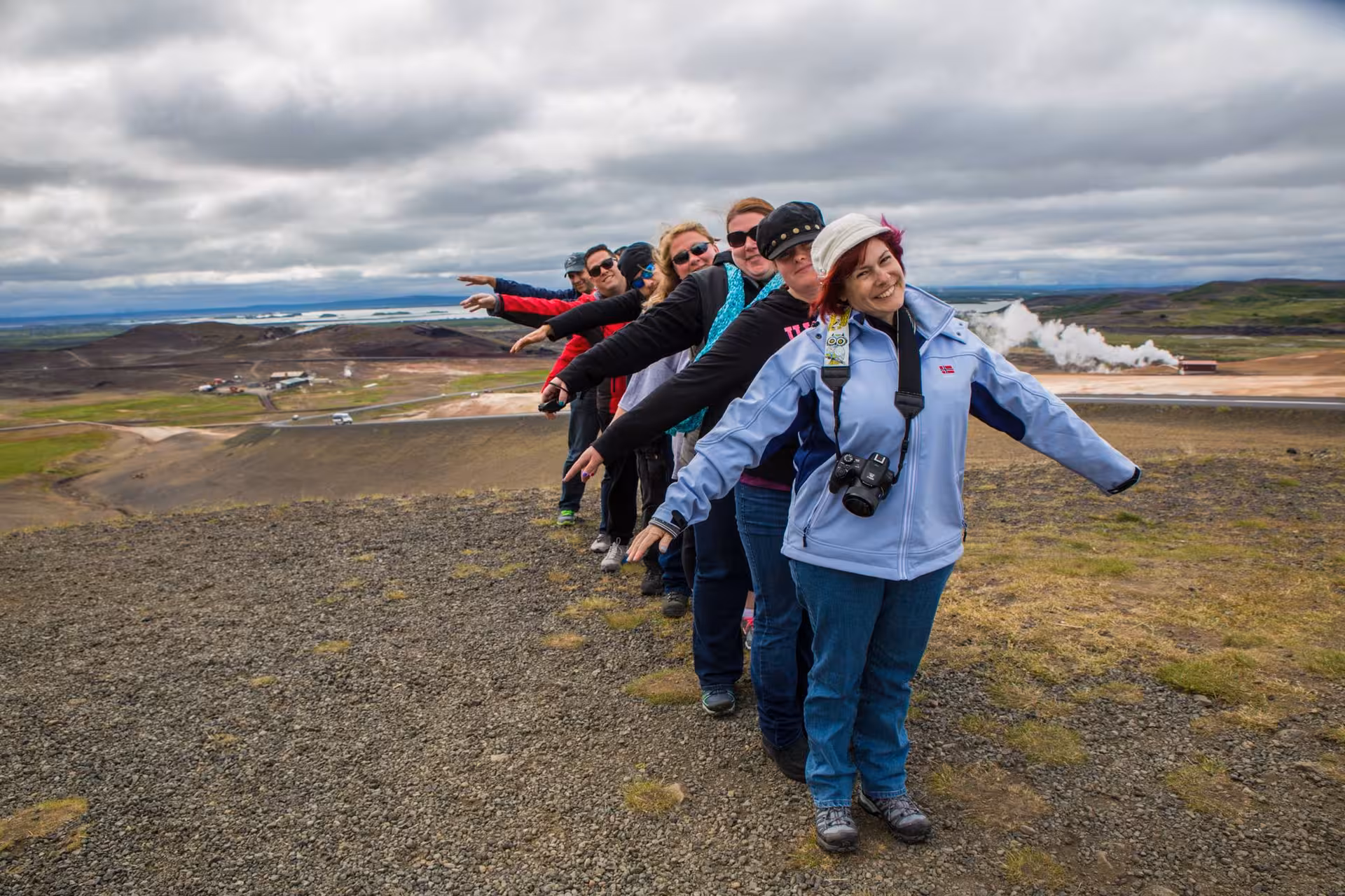 Group of tourists posing in a line with arms outstretched on volcanic landscape near Akureyri, Iceland
