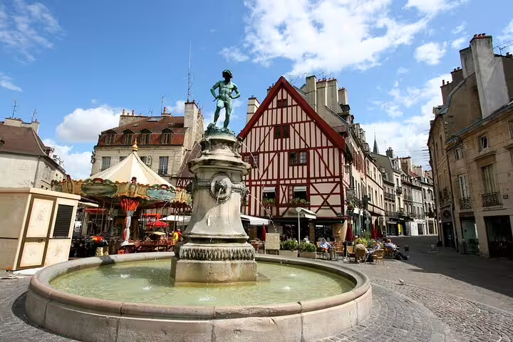 Fountain statue in Dijon town square with half-timbered building and carousel in background