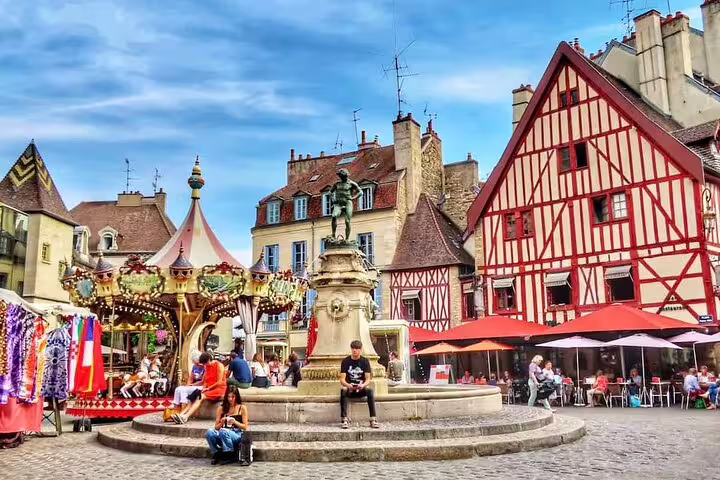 Dijon town square with fountain statue, carousel, half-timbered buildings and outdoor café terraces