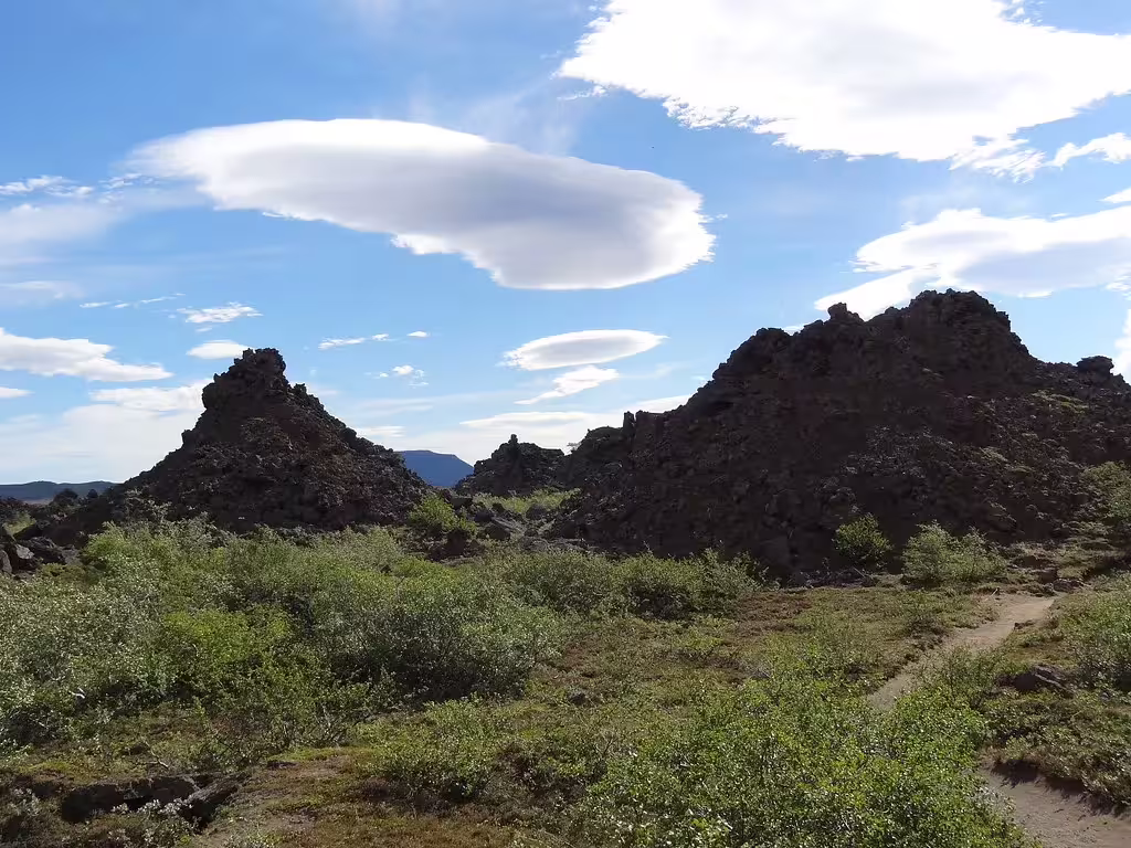 Rugged lava rock formations with green shrubs under blue sky with lenticular clouds, Diamond Circle Iceland