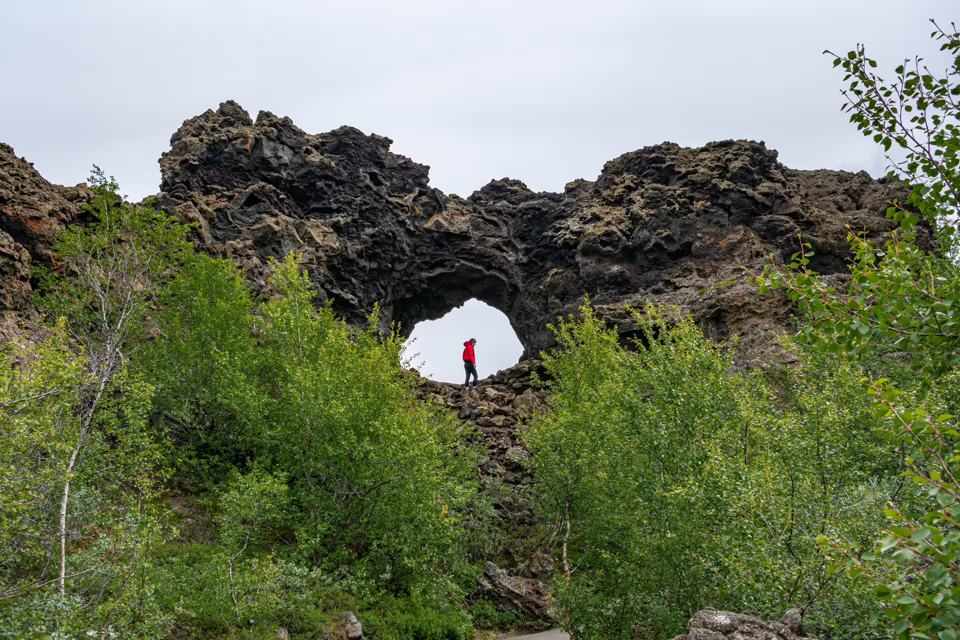 Hiker in red jacket standing inside volcanic lava rock arch at Dimmuborgir near Myvatn, Iceland