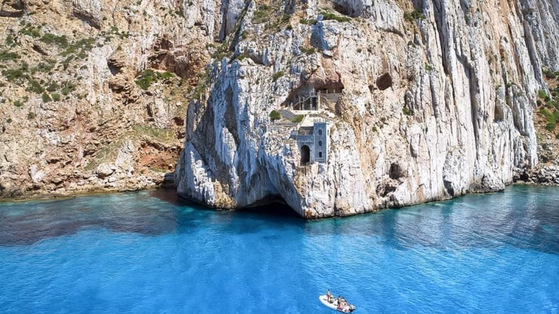 Dinghy approaching Porto Flavia's dramatic cliffside entrance with turquoise waters near Buggerru, Sardinia.