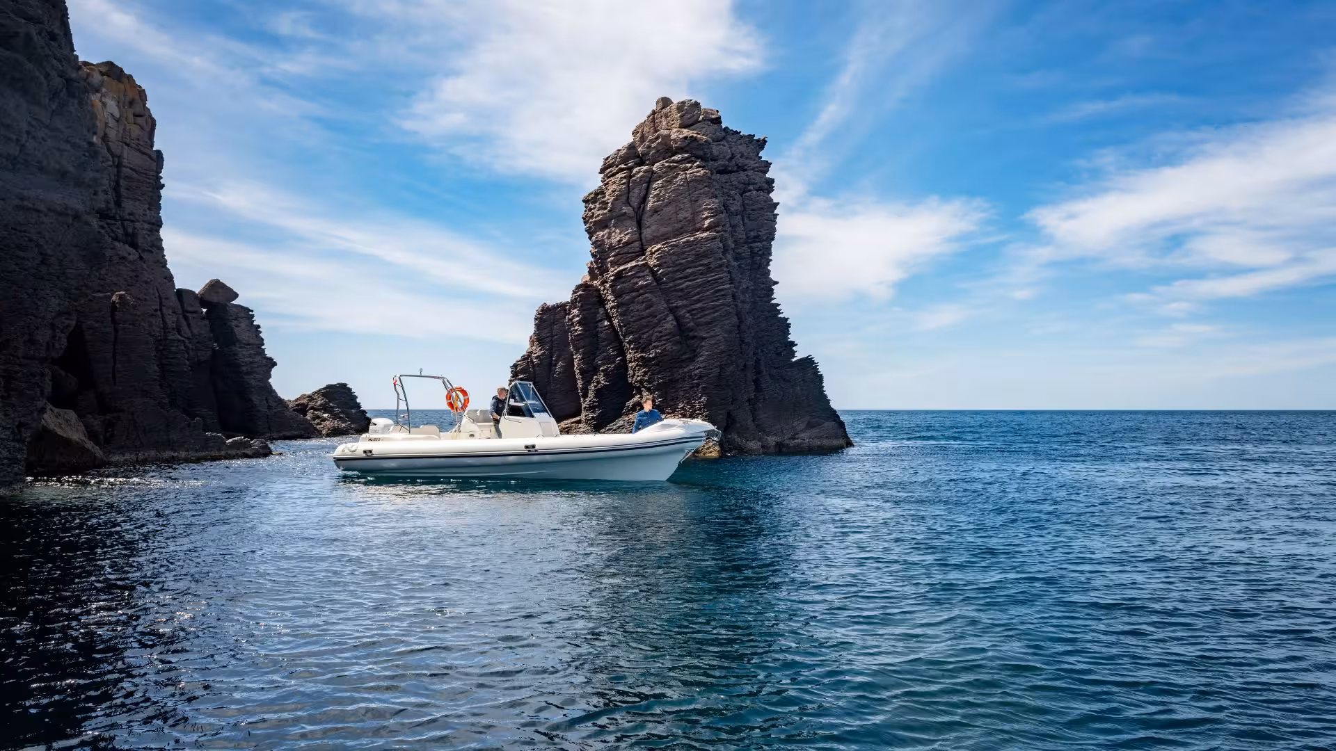 Dinghy navigating through striking rock formations in clear blue waters on the Carloforte to Sant'Antioco tour.