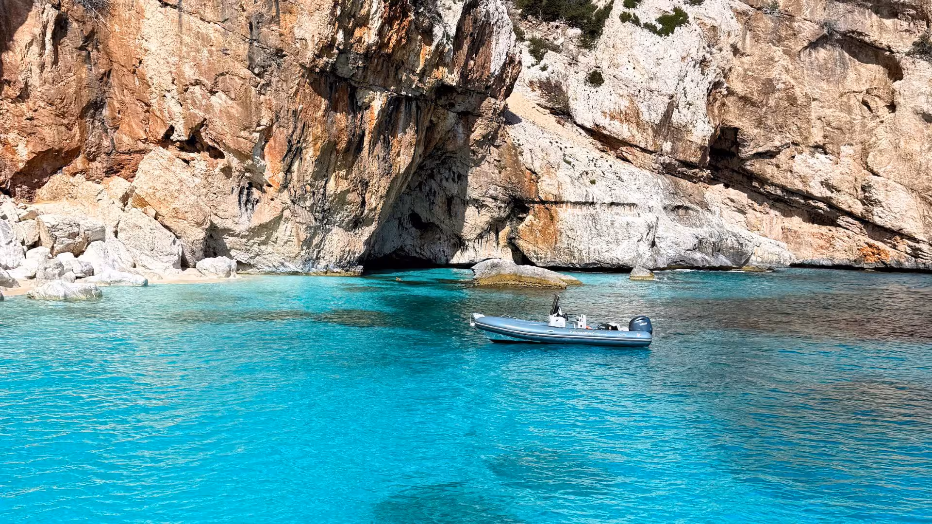 Dinghy floats on the turquoise waters of the Gulf of Orosei against a backdrop of rugged cliffs in Cala Gonone.
