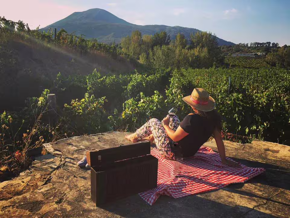 Guest relaxing on a picnic blanket with wine at sunset in a vineyard on the slopes of Mount Vesuvius near Naples
