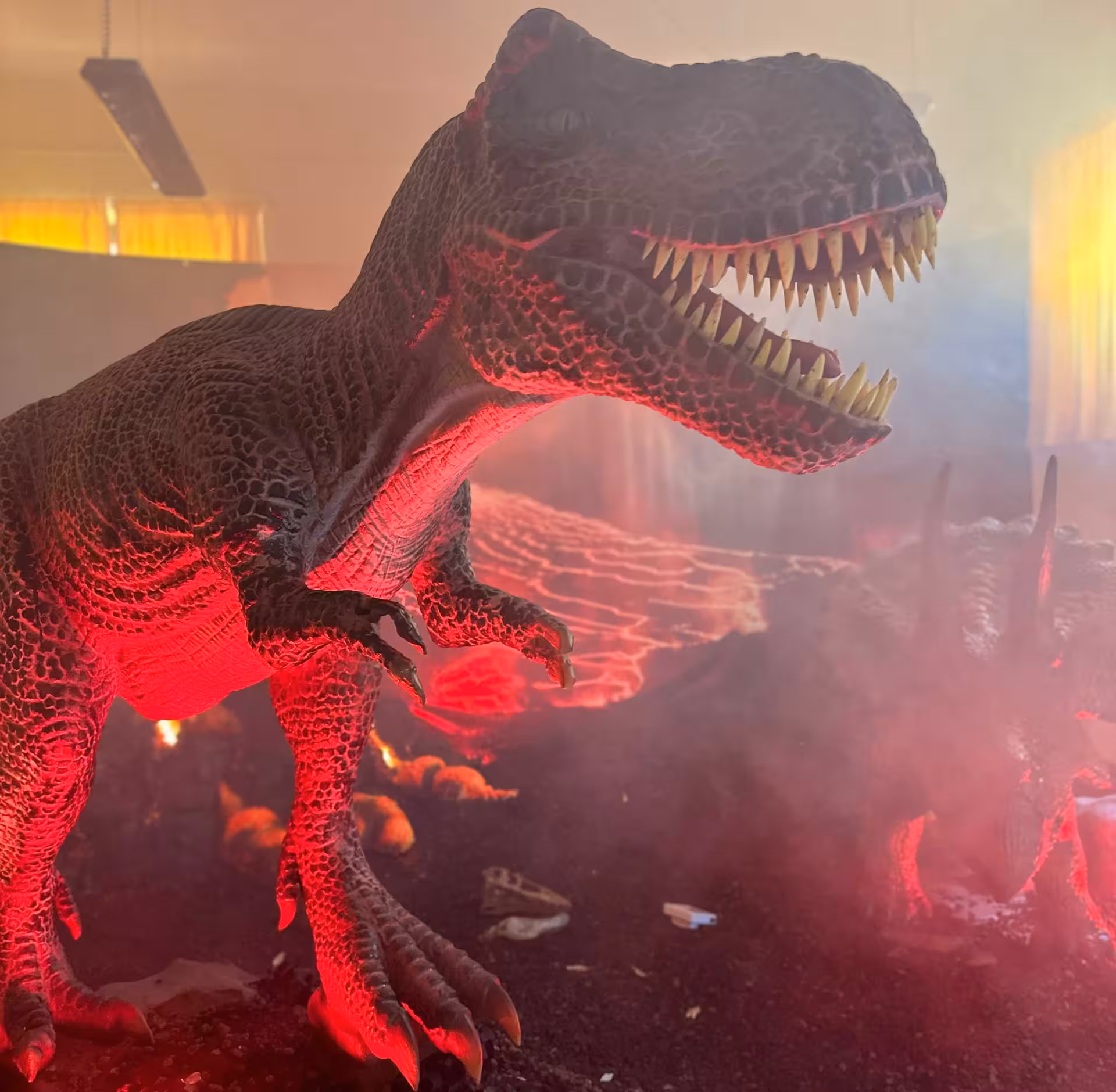 Ferocious dinosaur exhibit under red lighting and smoke effects at Porto Conte Park in Alghero.