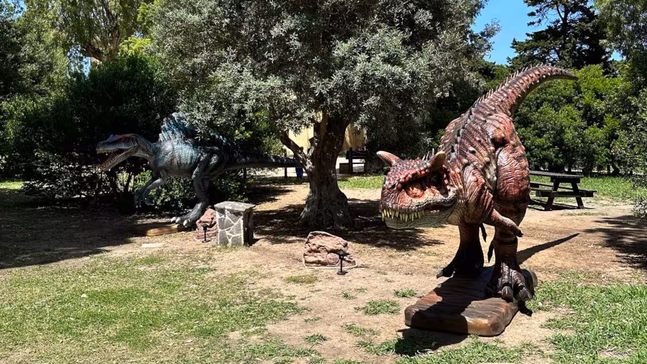 Two realistic dinosaur models under trees in Porto Conte Park, Alghero, offering a prehistoric adventure.
