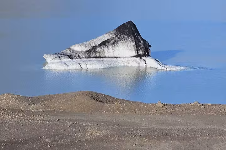 Sediment-covered iceberg floating in the calm blue glacial lagoon at Jokulsarlon, Iceland