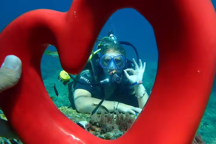 Diver framed by heart-shaped buoy signals OK underwater in Kusadasi's vibrant scuba diving tour experience.