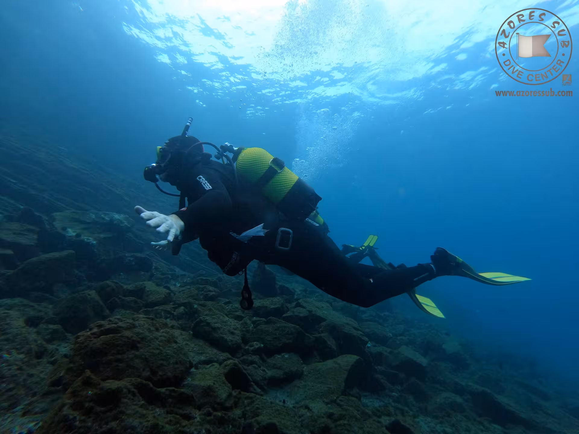 Diver gliding above rocky seabed on Baptism at Sea introductory scuba tour, calm blue ocean waters