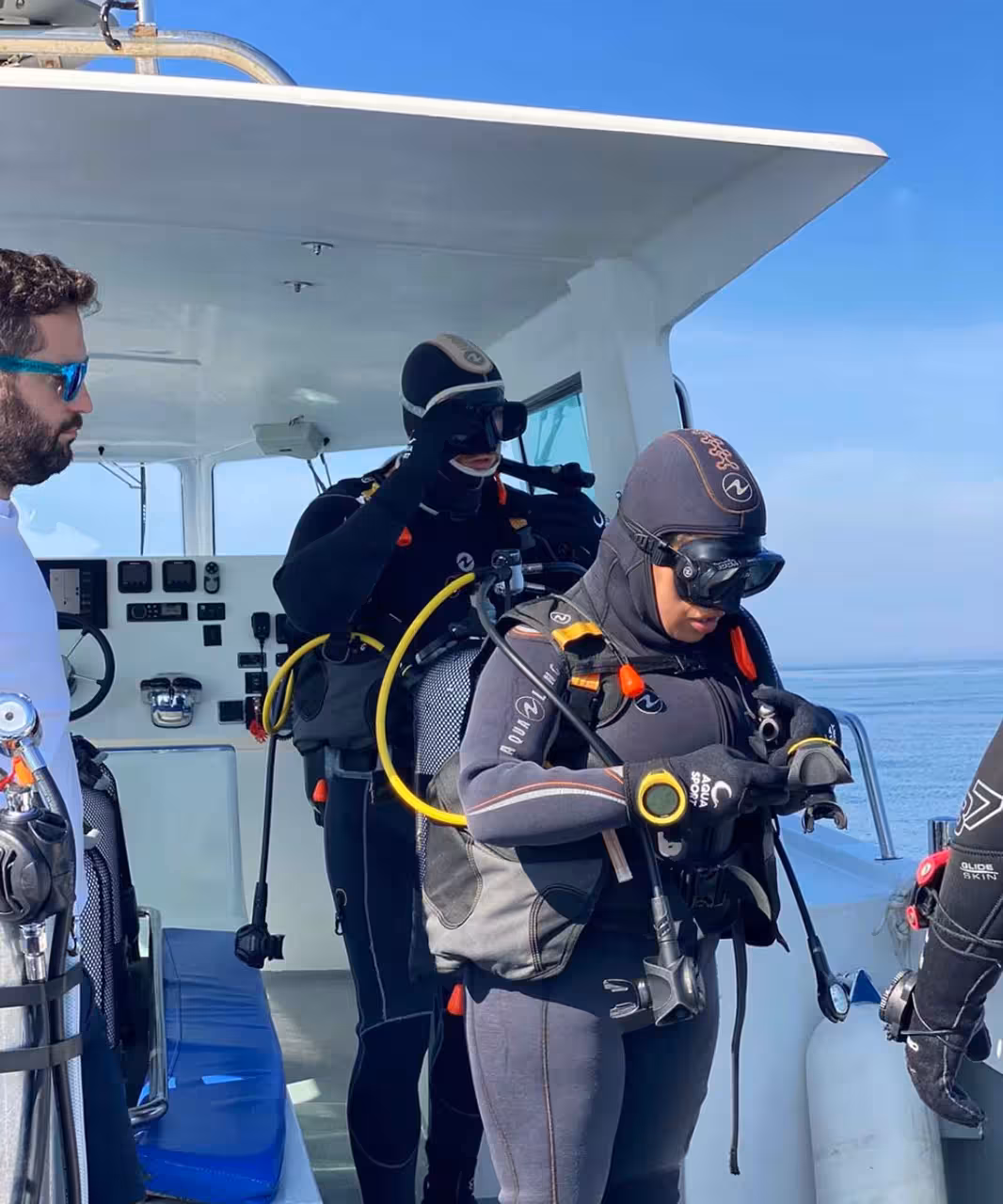 Divers in wetsuits checking scuba gear on a boat deck before the 1 DIVE guided ocean dive trip