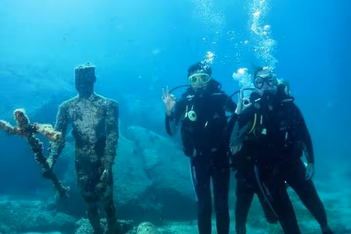 Two divers explore underwater statues, capturing the unique sights of a morning diving baptism experience.