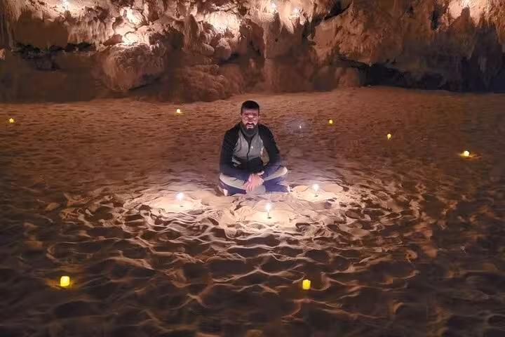 Guest seated by candles on sand inside Djara Cave, highlight of 3-day White Desert and Black Desert camping tour