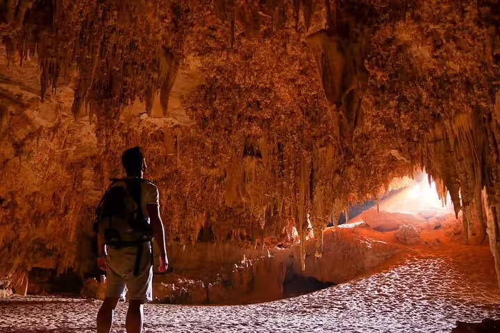Hiker exploring Djara Cave stalactites and sandy floor, essential experience on Egypt desert camping package