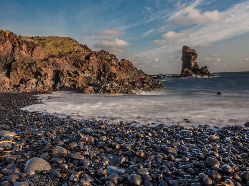 A picture of Djúpalónssandur with the ocean and a rock formation in the background.