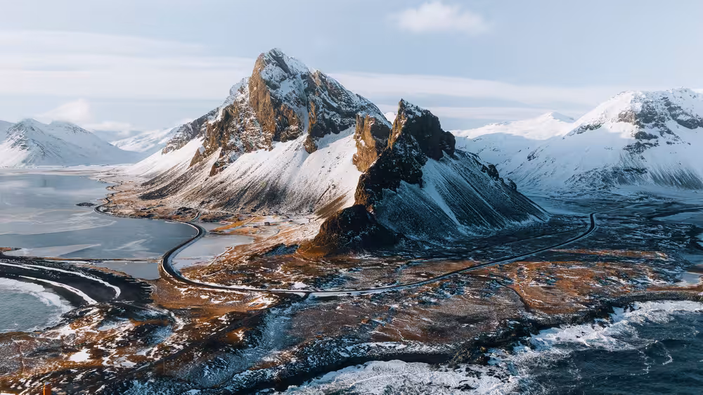 Aerial view of snow-capped mountains and winding coastal road near Djupivogur, Iceland in winter
