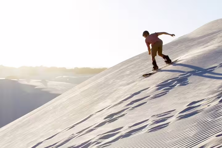 Adventurer sandboarding down a sunlit dune during a thrilling desert safari in Doha.