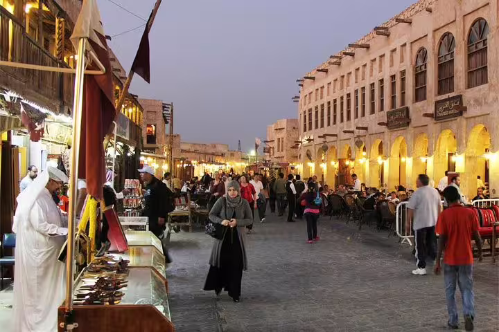 Bustling Souq Waqif in Doha at dusk, lively market atmosphere with shops, local vendors, and visitors exploring.