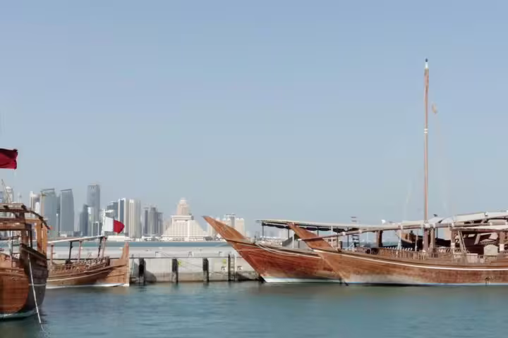Traditional wooden dhows in Doha harbor with a skyline backdrop on the Doha transit city tour from Hamad Airport.