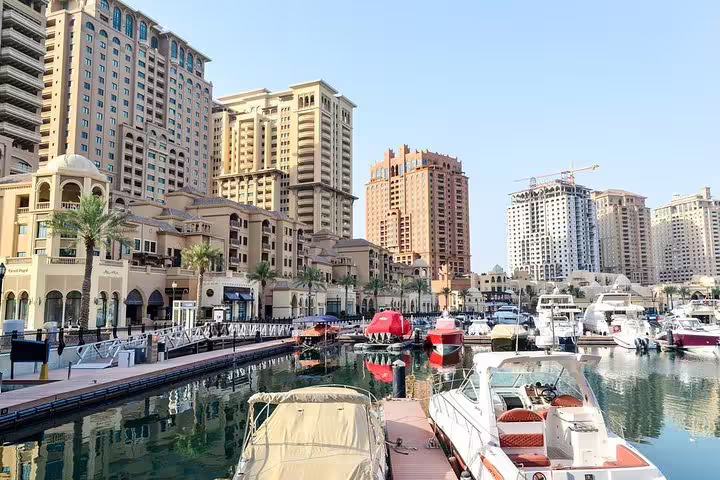 Luxurious yachts docked at The Pearl-Qatar marina amidst high-rise buildings, highlighting Doha's modern architecture and lifestyle.