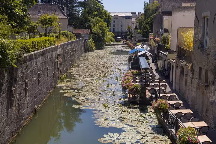 Canal in Dole France lined with lily pads, outdoor café seating, and stone buildings on a sunny day