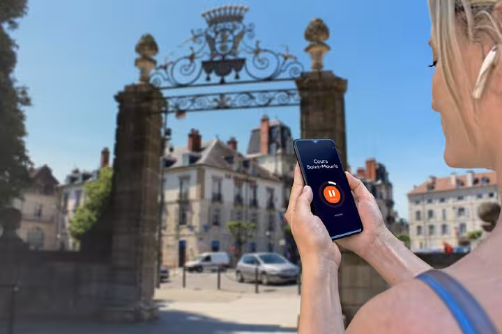 Woman holding smartphone with audio guide app at ornate Cours Saint-Mauris gate in Dole, France