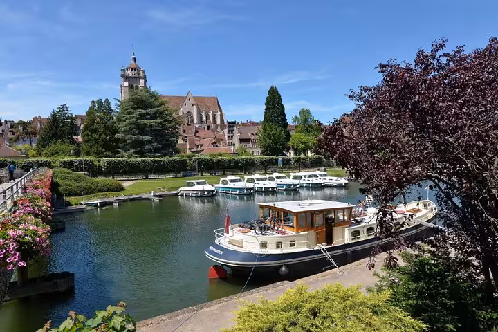 Boats moored on the Doubs River in Dole, France, with a historic church and town buildings in the background