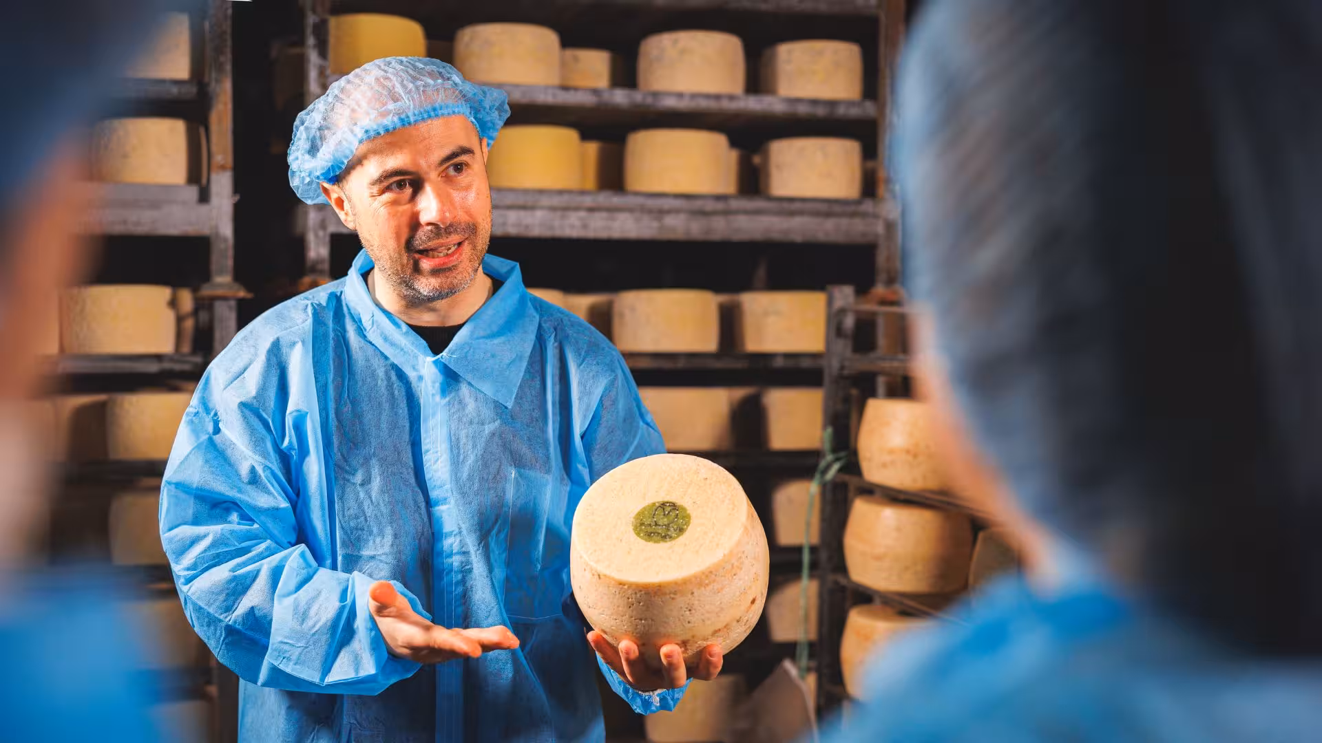 Cheese maker presenting a cheese wheel in a Dolianova factory tour, emphasizing artisanal craftsmanship.